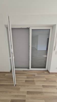 Innenansicht einer Balkontür mit einem heruntergelassenen, hellgrauen Rollladen zur Verdunkelung und Wärmedämmung.