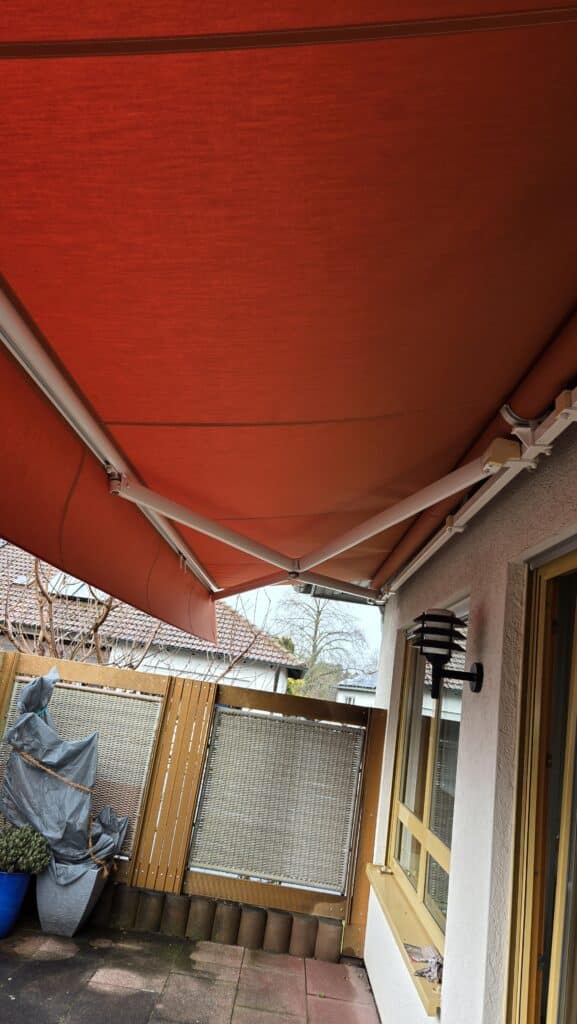 Neu bespanntes Markisentuch in Orange bei der Montage auf einer Terrasse