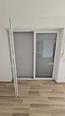 Innenansicht einer Balkontür mit einem heruntergelassenen, hellgrauen Rollladen zur Verdunkelung und Wärmedämmung.