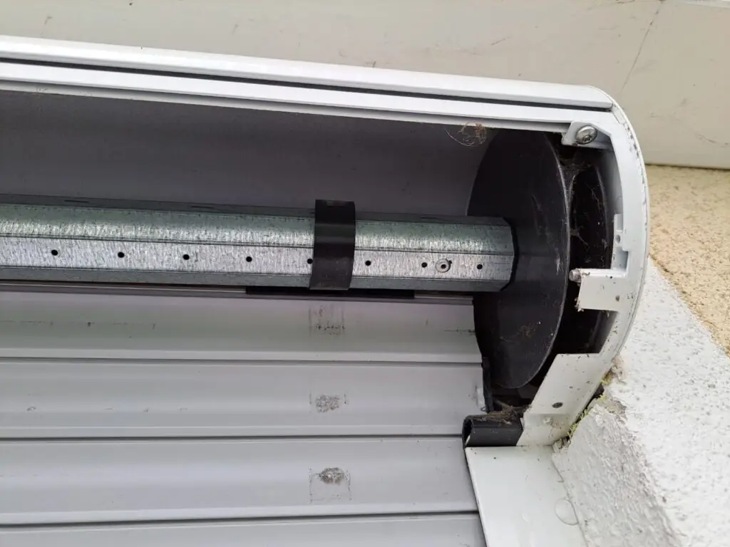 Geöffnete Ansicht eines Vorbau-Rollladens mit Blick auf die Wickelwelle und den teilweise aufgerollten Rollladenpanzer im Aluminiumgehäuse.“