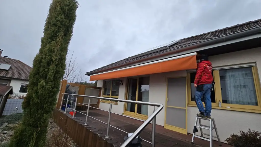 Montage eines neuen orangefarbenen Markisentuchs auf einer Terrasse.